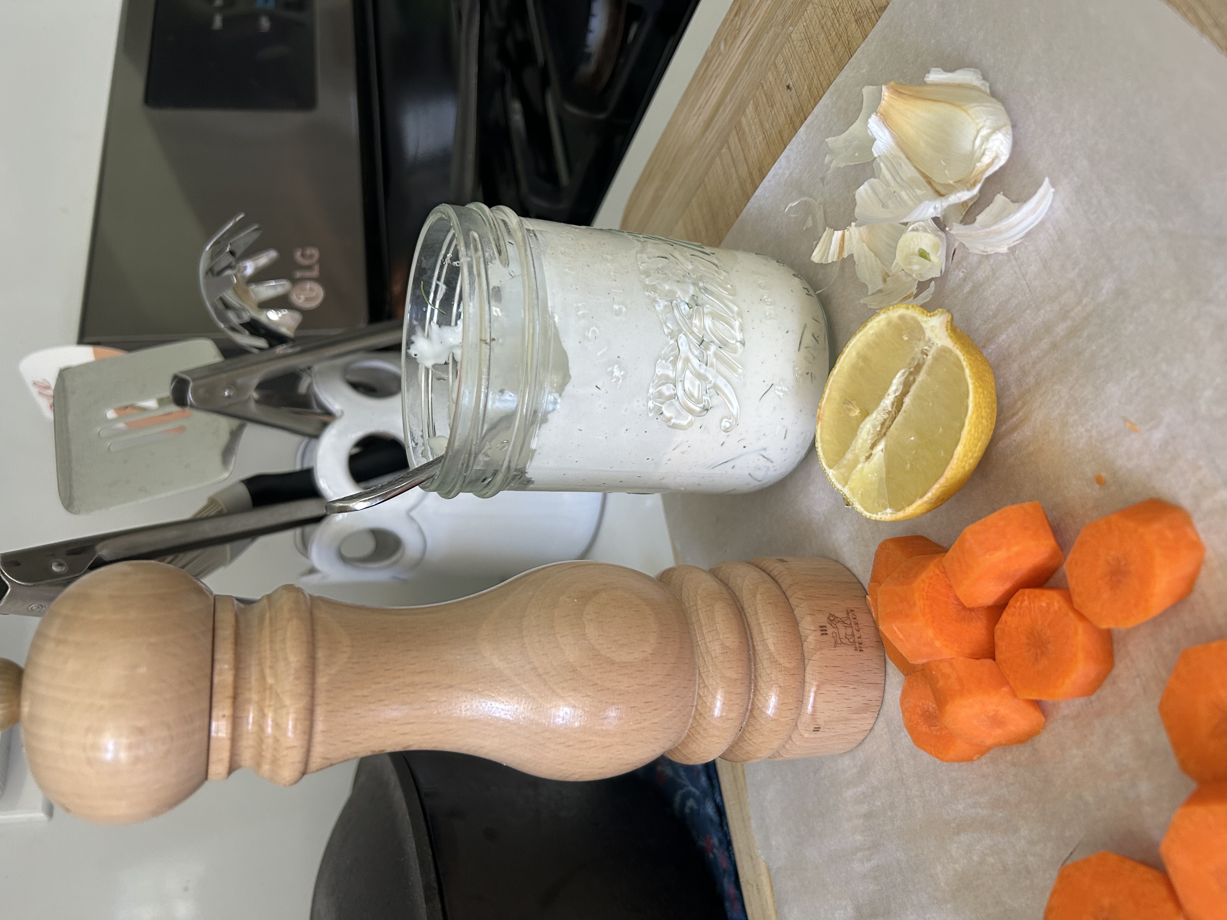 Homemade ranch dressing in a jar beside carrots, lemon, garlic, and a pepper mill